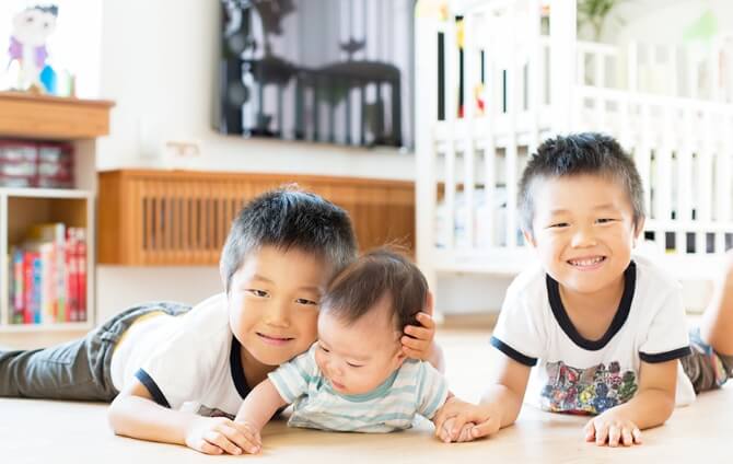 桧の床で寝そべって笑顔を向ける双子の兄弟と赤ちゃん